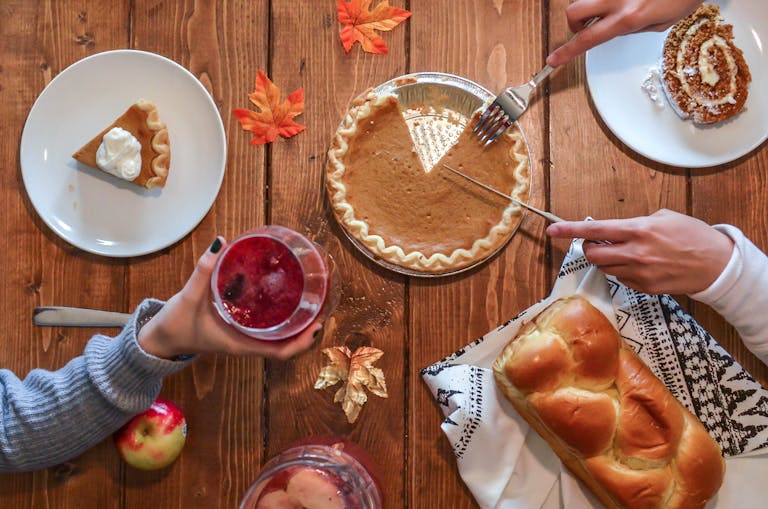 Cozy autumn table setting with pumpkin pie, bread, and drinks. Perfect for Thanksgiving vibes.