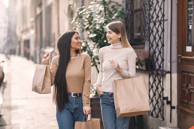 Two cheerful women carrying shopping bags while strolling down a sunny street.
